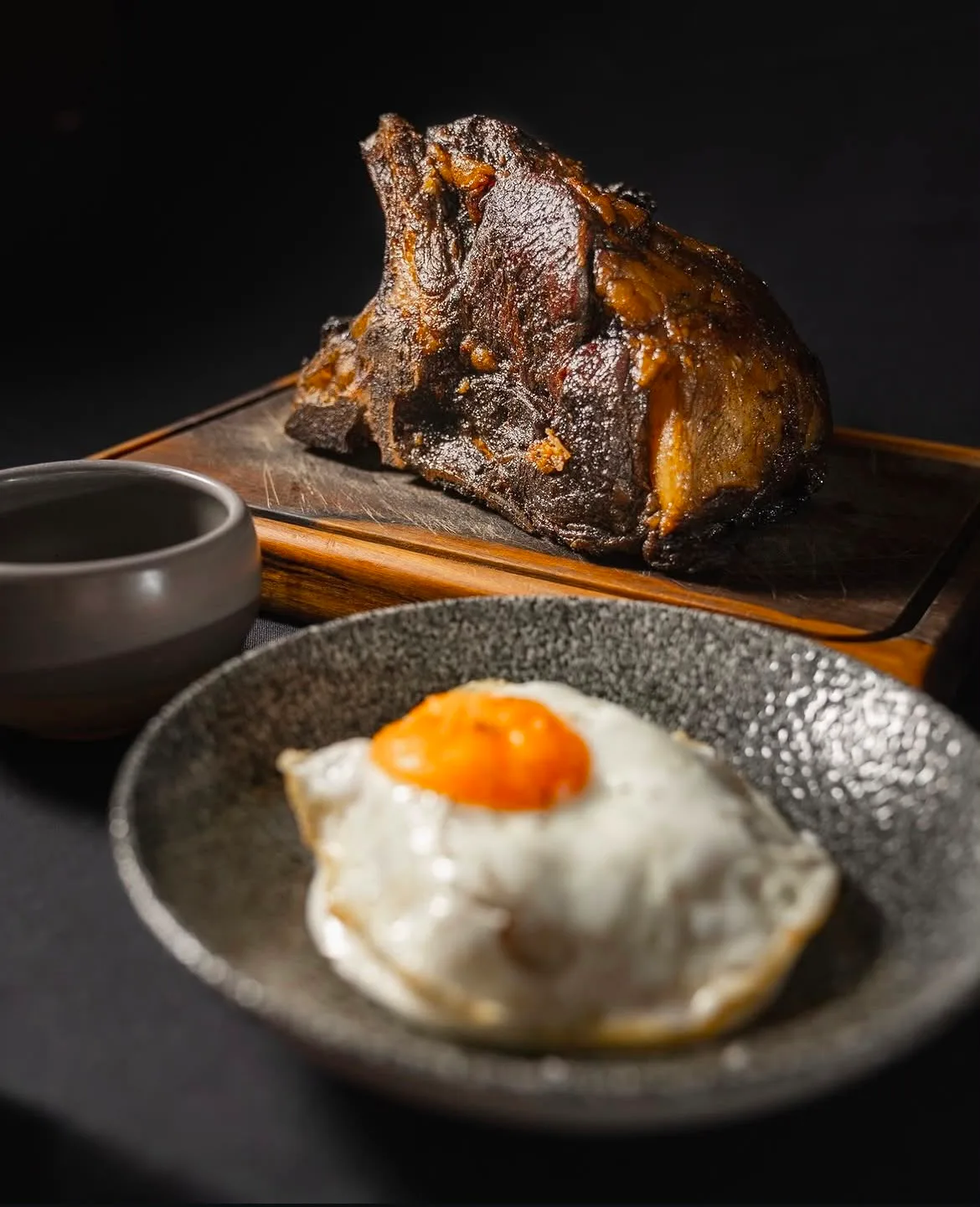 Carne braseada a fuego lento en tabla de madera, con huevo frito de campo